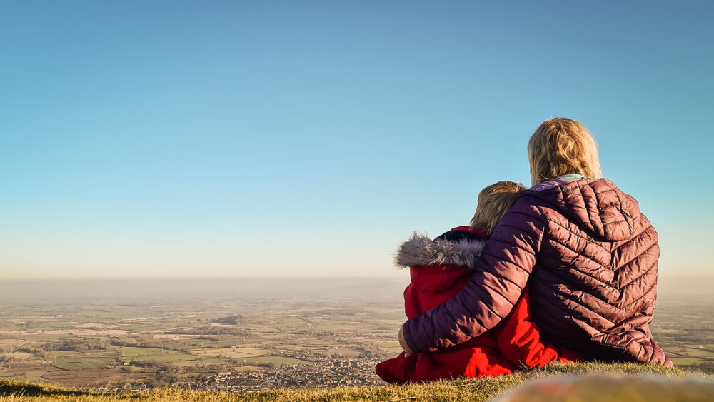Pickle and Mommy sitting together on the grass overlooking the views of Malvern from North Hill, the Malvern Hills