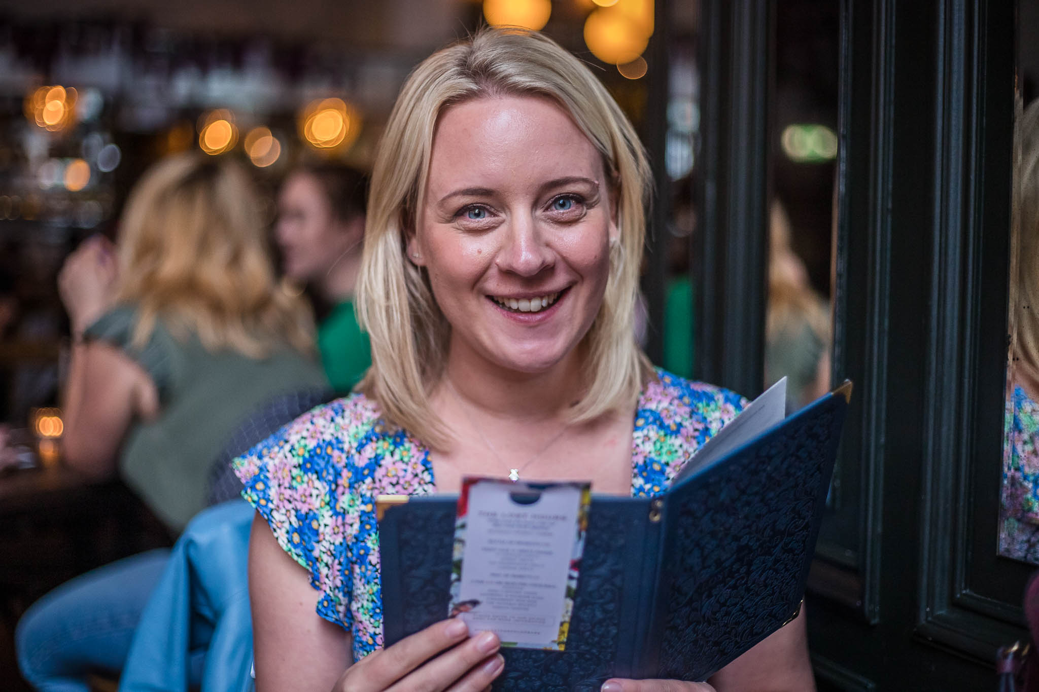 Woman reading a drinks menu looking into the camera and smiling at The Lost and Found, Birmingham.