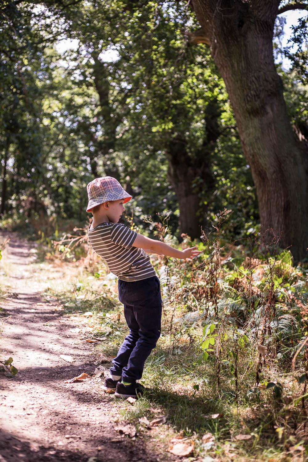 Child bending backwards gesturing to the woodland plants surrounding him.