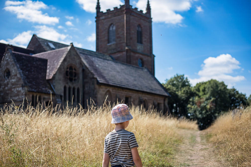 Child standing in front of the church with long dry looking grass
