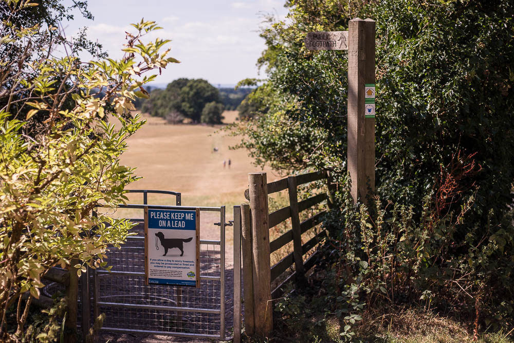 Public footpath signpost pointing towards a kissing gate leading to the Hanbury estate